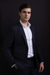 A professional profile photo for a young solo entrepreneur wearing a jacket and open collar. Dark background.