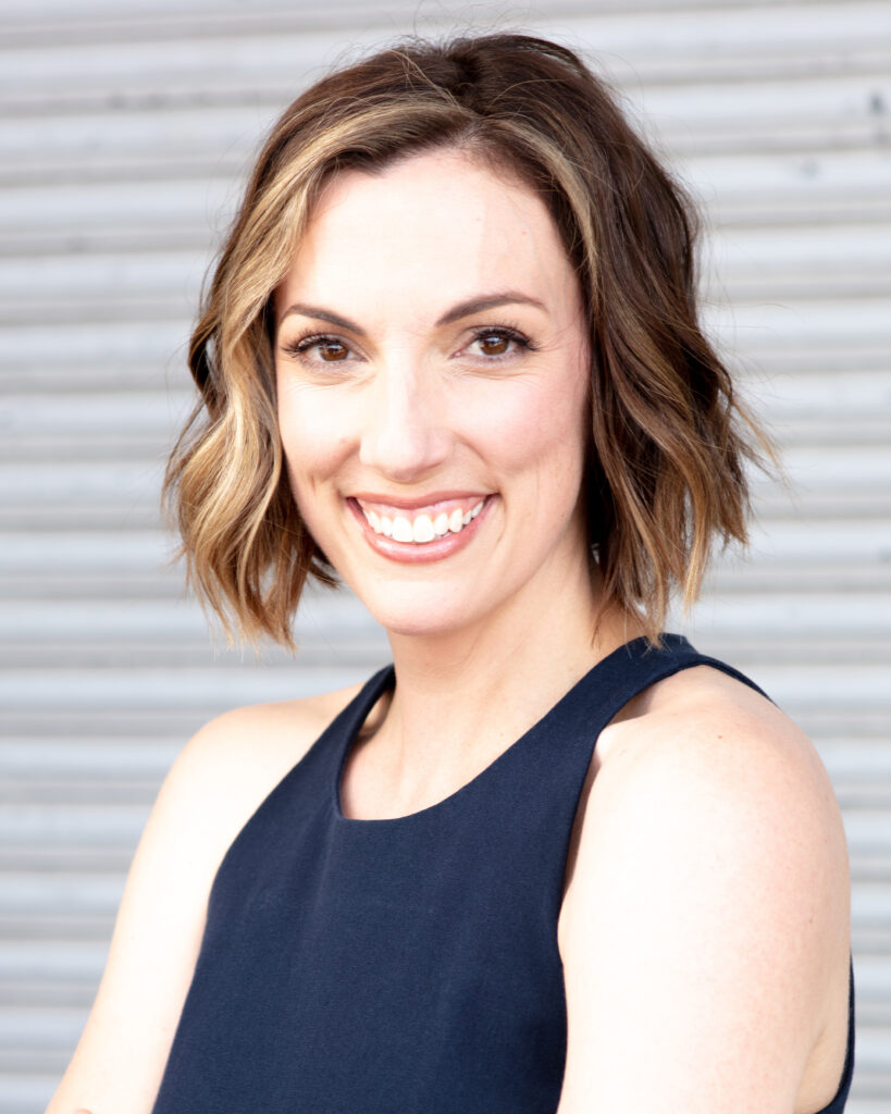 Headshot for young female real estate professional shot against a commercial corrugated steel background. Informal, smiling.