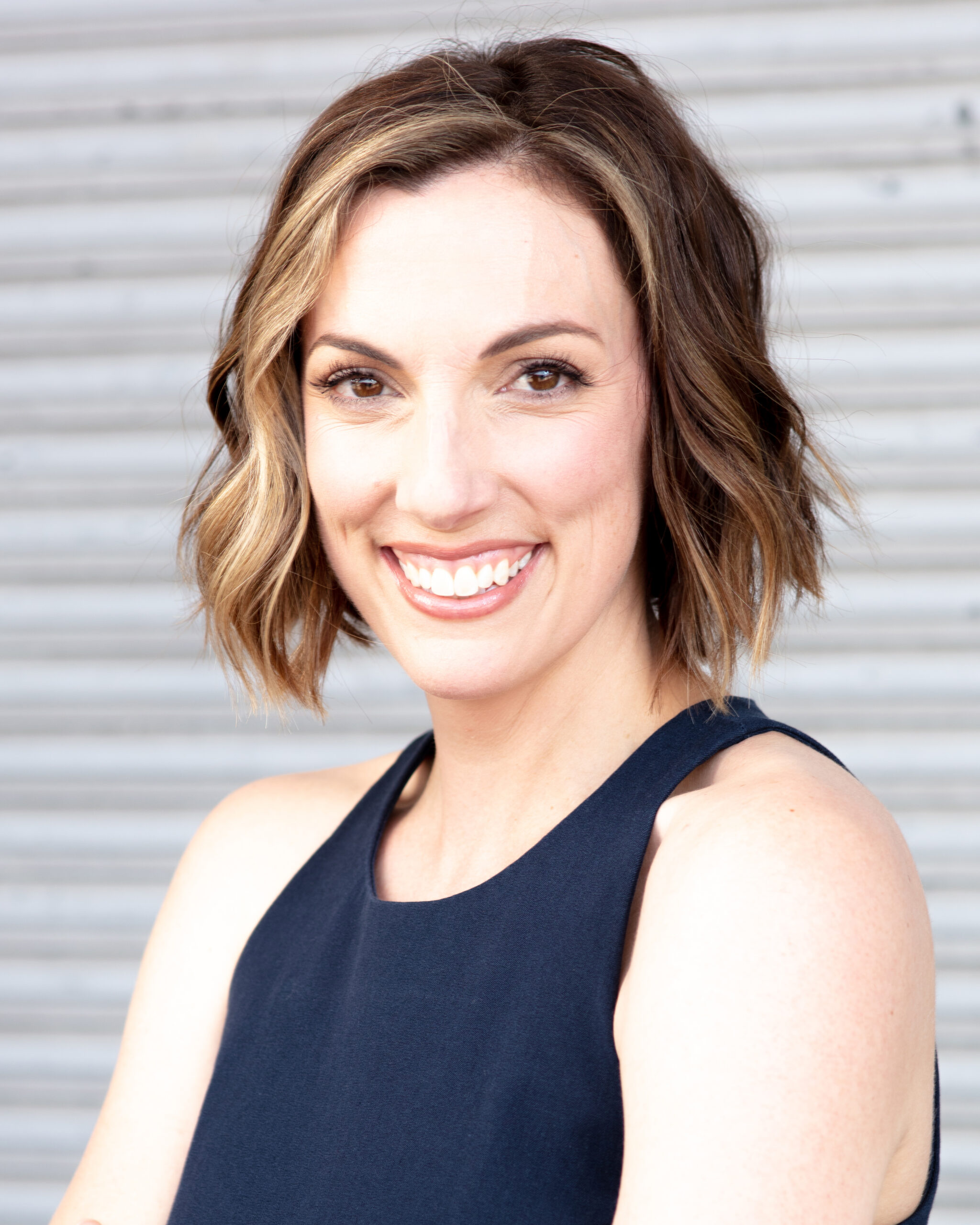 headshot-real-estate-agent-Gerard-Harrison-photographer-Houston Headshot for young female real estate professional shot against a commercial corrugated steel background. Informal, smiling.