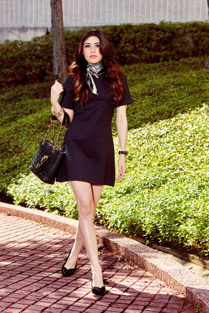 Model in little black dress by Work in Process and elegant accessories, walks on brick sidewalk near Galleria Houston.