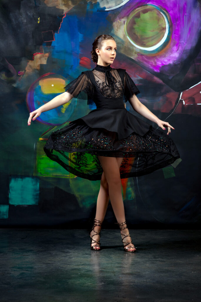 Model portfolio photo of female model dancing in beaded couture cocktail dress in front of futuristic abstract mural.