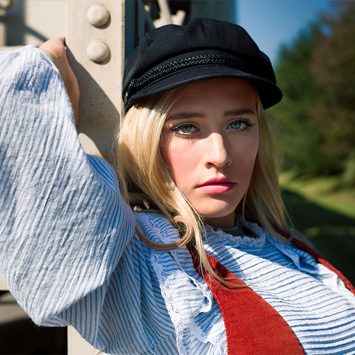 Modeling portfolio photo of blond model with black cap, standing beside a freight train car.