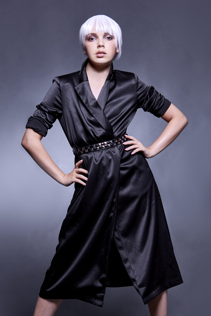 Model portfolio photography by Gerard Harrison Model with white hair strikes angular hands on hips pose in black satin dress for modeling portfolio.