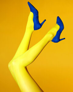 A woman holds pretty legs and blue suede in the air against a gold background. Part of a romantic fashion campaign.